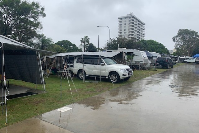 A white 4WD is parked under a tarp at a campground.