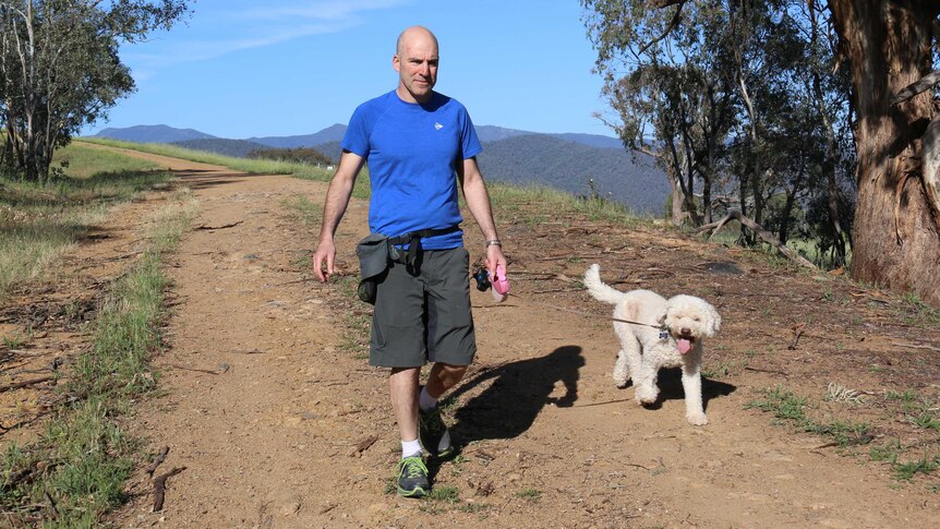 A man walks his small, fluffy white dog in a nature reserve.