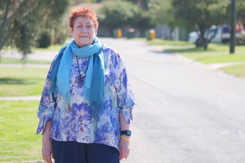 A woman in a bright coloured shirt standing with a street in the background.