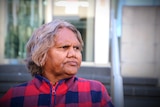 A woman wearing a red and blue cardigan stands outside a court building