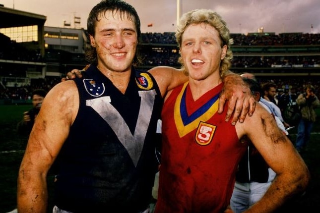 Former VFL/AFL players Tony Lockett and Dermot Brereton stand with arms around each others shoulder.