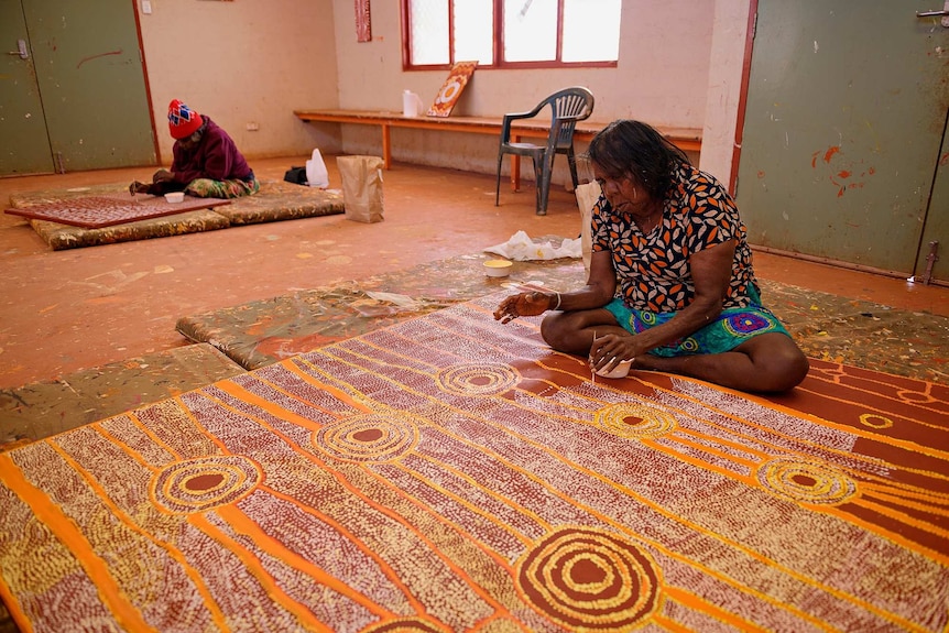 Artist Mary Brown paints while sitting on the floor in a workshop.