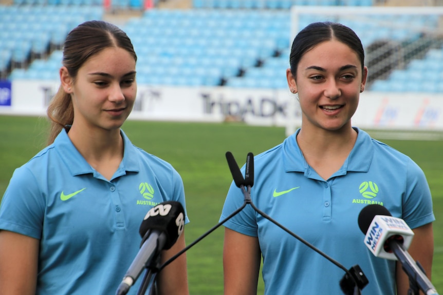 Indiana and Zinaya dos Santos speak from the podium at WIN Stadium with the pitch behind them.