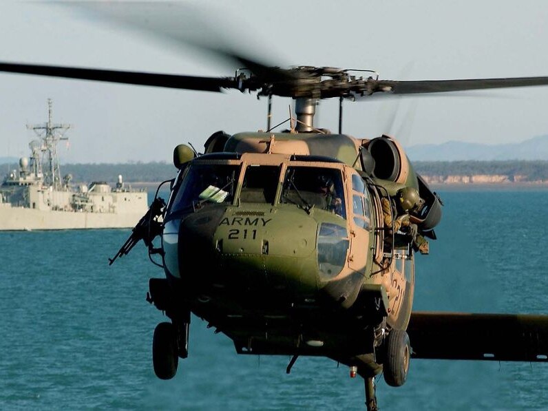 A military helicopter mid air with warship in background