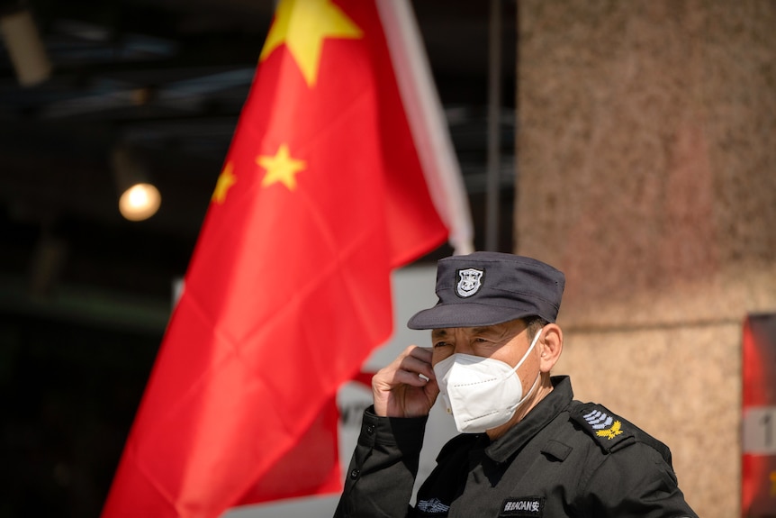 A security guard wearing a face mask stands near a Chinese flag.