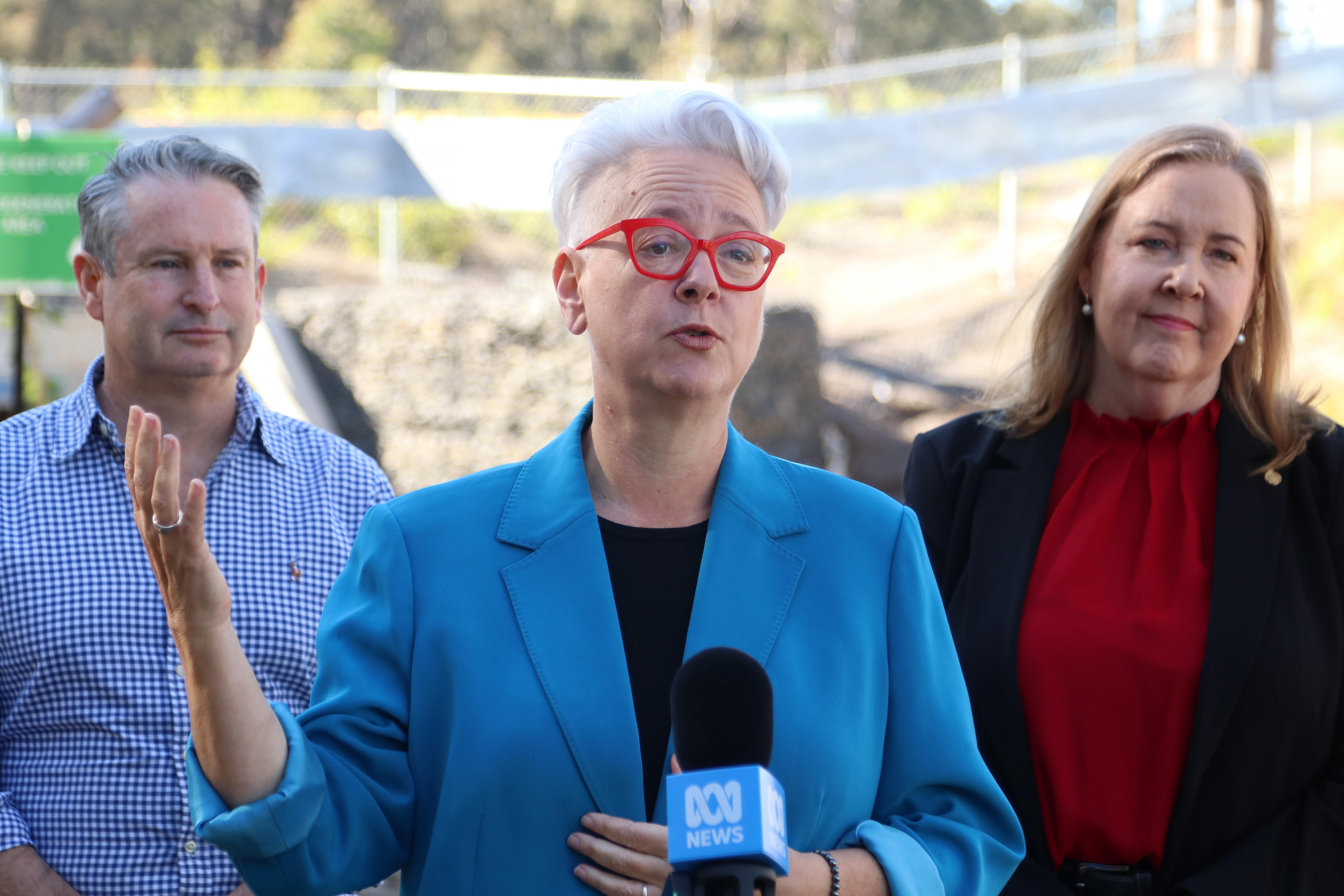 one man with grey hair and two woman speaking outside box culvert