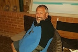 Shane Cregan sitting on an outdoor seat next to a house at night, smiling.
