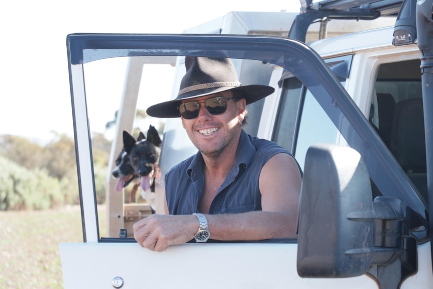 Smiling man in ute window frame with dogs in background
