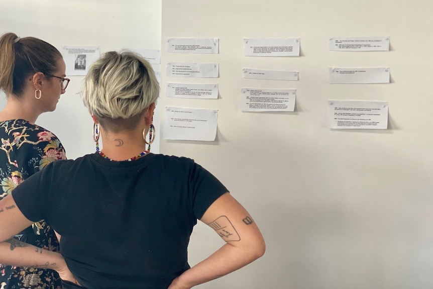 Medium shot of the backs of two caucasian women looking at paper cut outs stuck on 