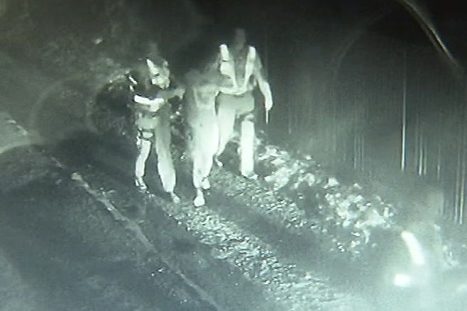 Black and white CCTV of a man being arrested by police officers in a laneway.