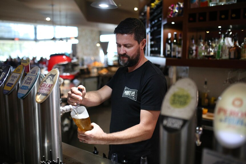 A man with a beard pouring a beer into a pint in a restaurant.