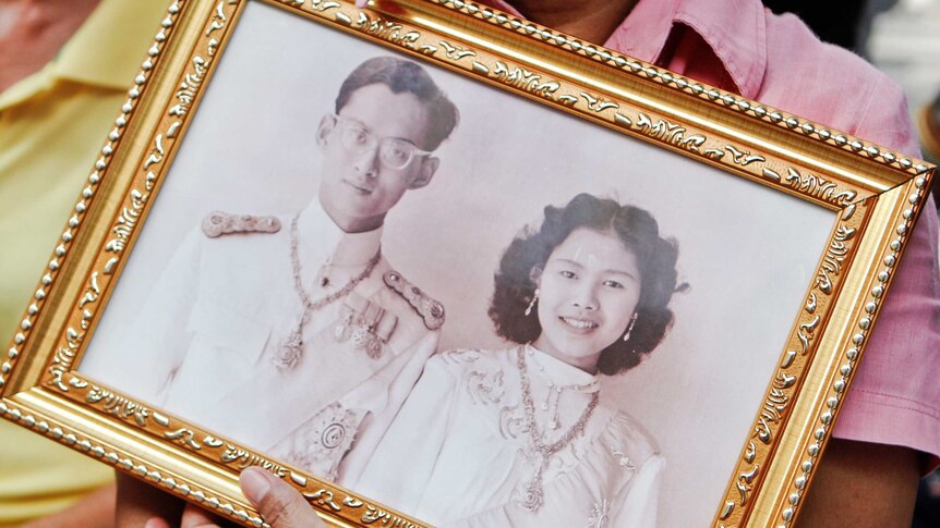 A well-wisher holds a black and white photo of Thailand's King and Queen.