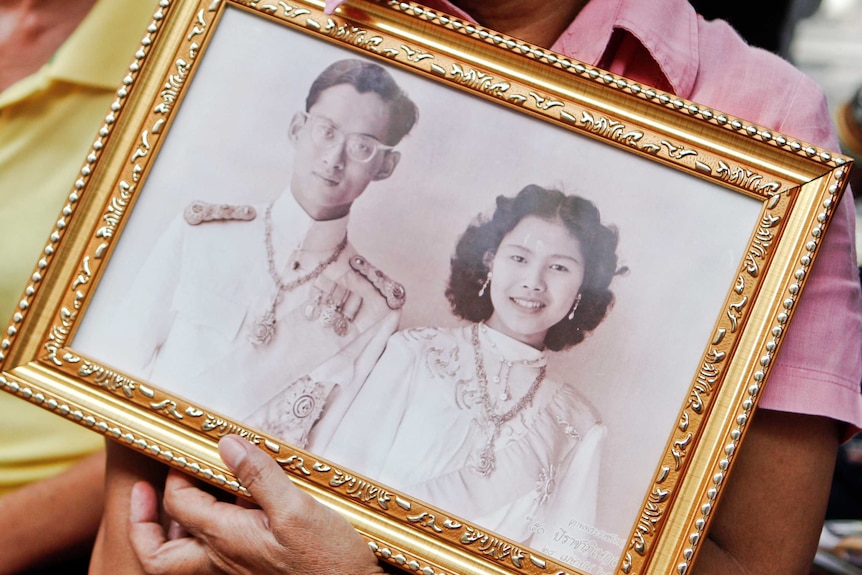 A well-wisher holds a black and white photo of Thailand's King and Queen.