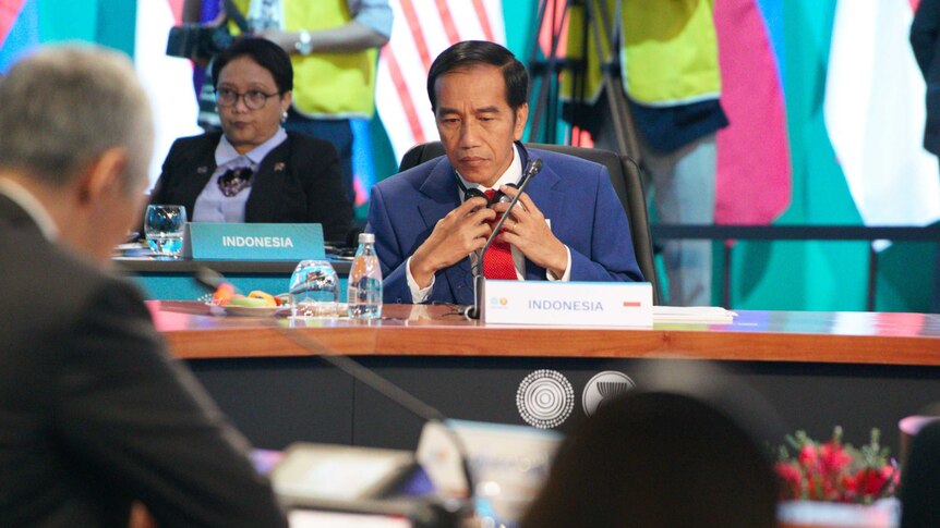 The Indonesian President looks down as he sits behind a desk during the ASEAN summit.