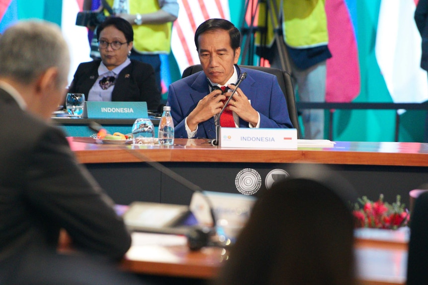 The Indonesian President looks down as he sits behind a desk during the ASEAN summit.