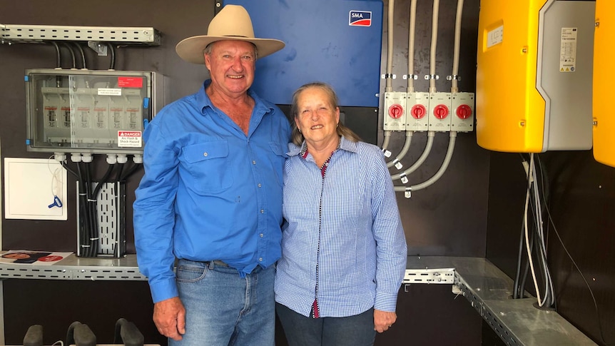 Man with a country hat stands next to a woman next to batteries, wires and energy monitoring devices