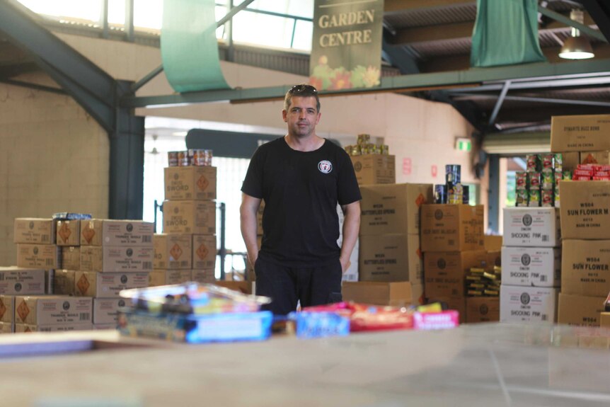 A man in front of boxes of fireworks.