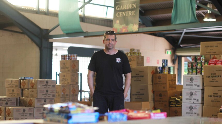 A man in front of boxes of fireworks.