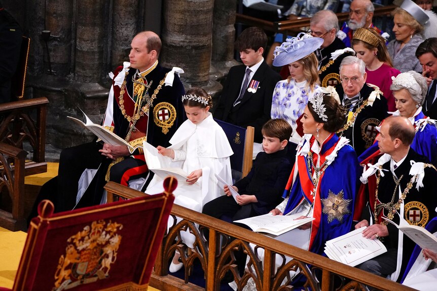The Prince of Wales, Princess Charlotte, Prince Louis, the Princess of Wales sitting in a pew holding programs.