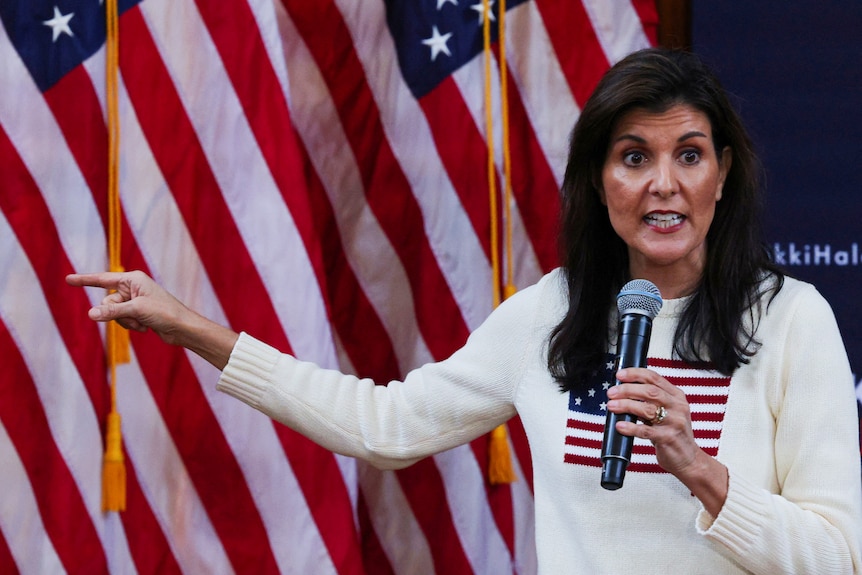 Nikki Haley speaks on stage wearing a white jumper with a US flag on it.
