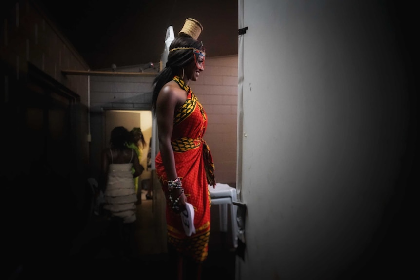 A young woman in traditional Maasai and Kiyuku dress smiles as she walks on to a stage.