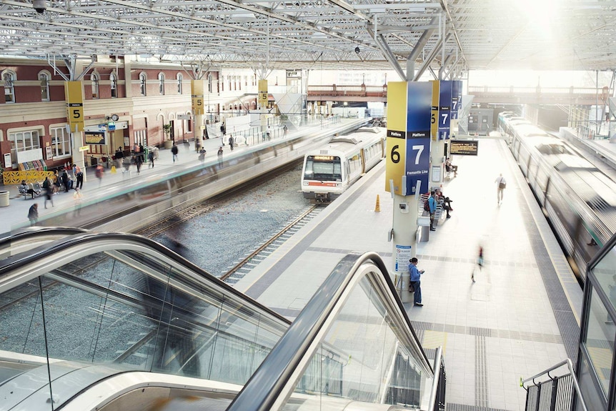 A wide shot from the top of the escalators showing the platforms at Perth train station with trains pulling in and out.