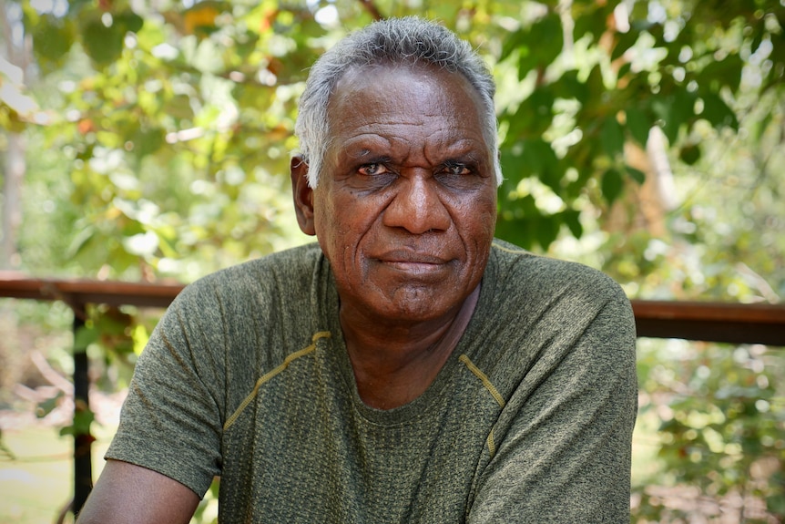 An Aboriginal man sits outside with a serious expression.