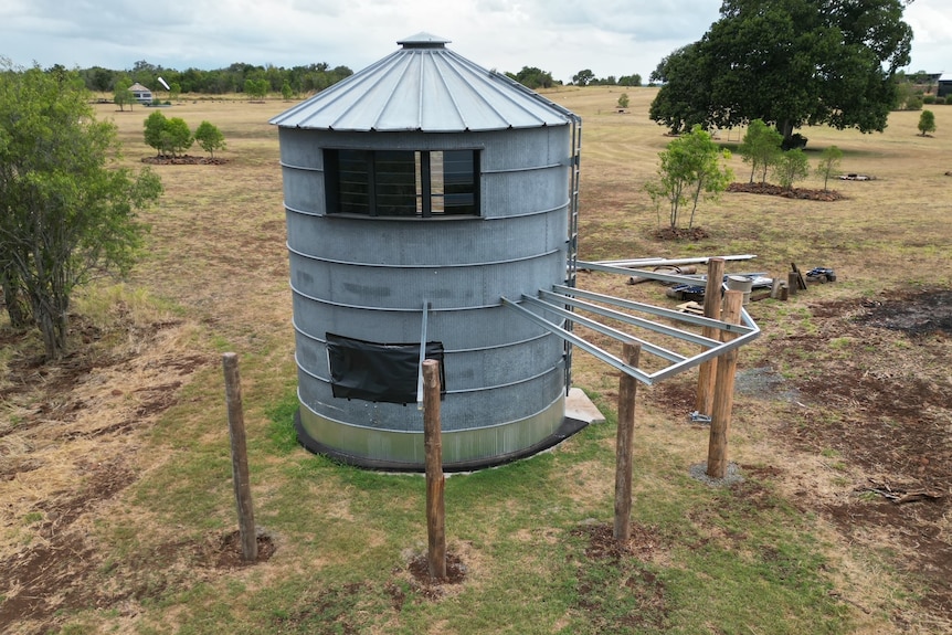 A grey silo sits in a paddock
