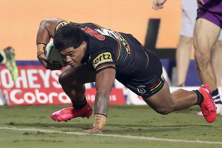 A Penrith Panthers NRL player scrambles over the line to score a try against the Melbourne Storm.