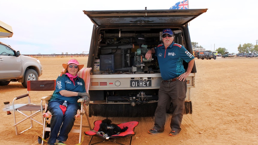 A couple leaning on the back of their ute, in the red outback sand of western Queensland.
