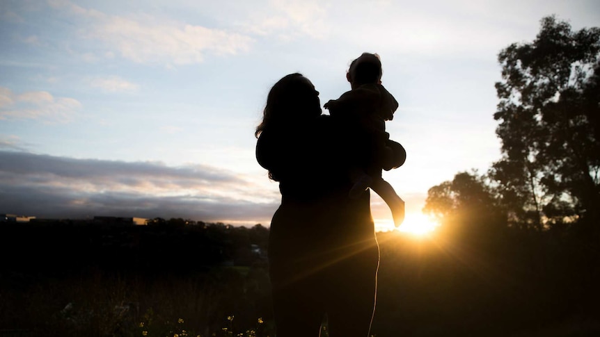 Silhouette of a woman holding her baby outside as the sun sets.
