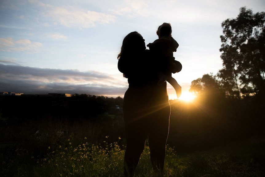 Silhouette of a woman holding her baby outside as the sun sets.