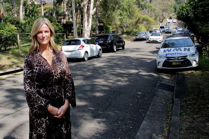 A woman standing in front of a street with police cars parked in it.