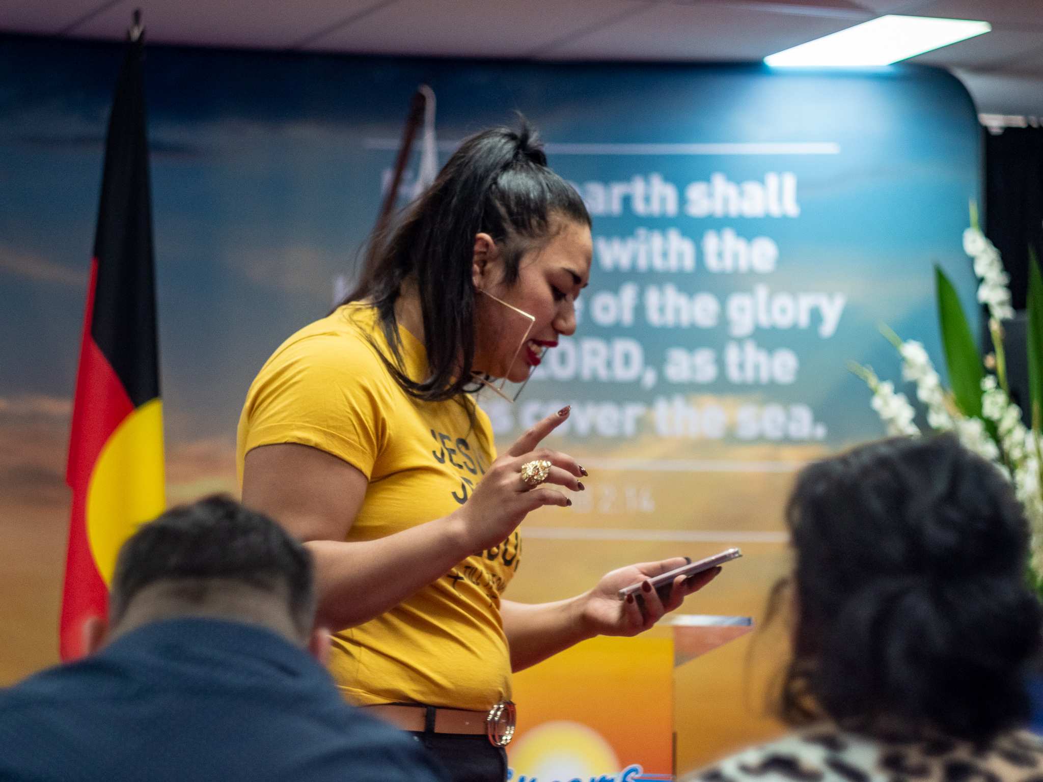 Ana Makahununiu standing in front of a small audience, is reading a sermon from her iphone.