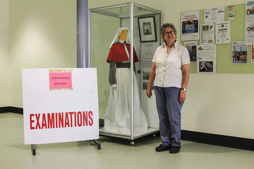 woman standing and smiling next to a nursing uniform exhibition and a sign saying EXAMINATIONS