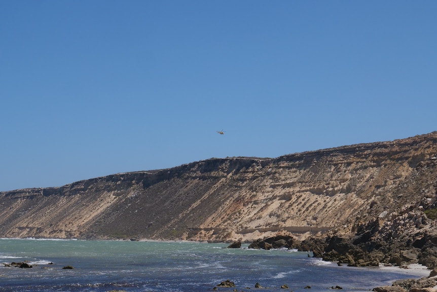 A cliff with a helicopter flying over it in the distance