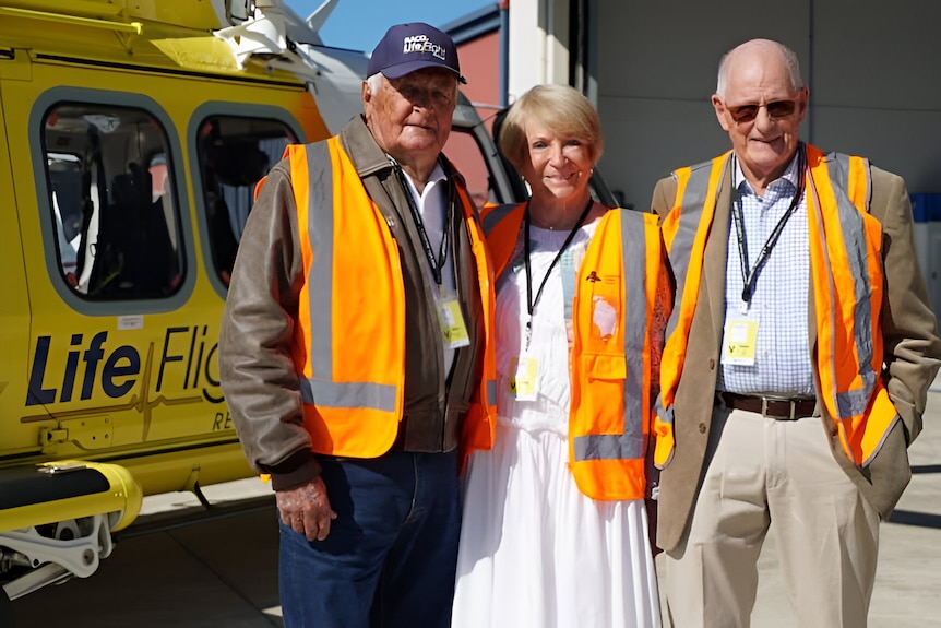 A woman standing between two men in front of a helicopter at the airport