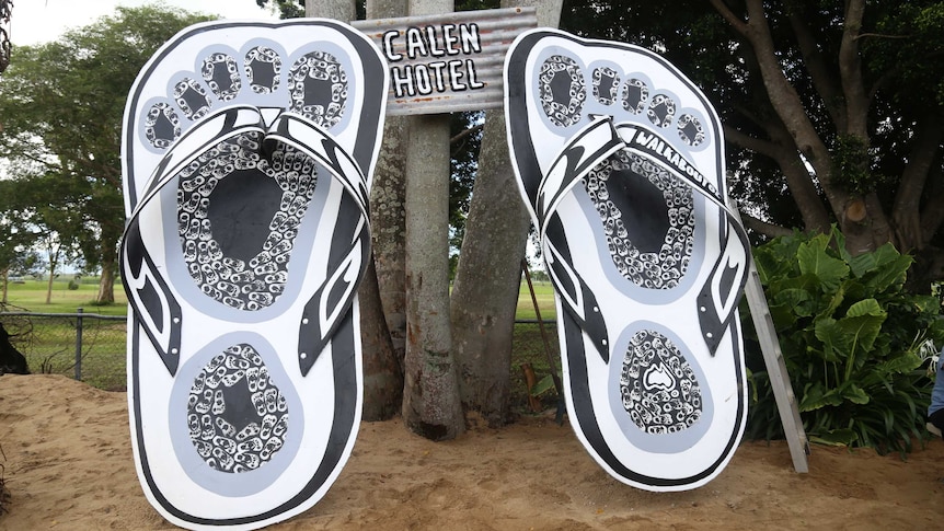 A large pair of black and white thongs, sitting against a tree.