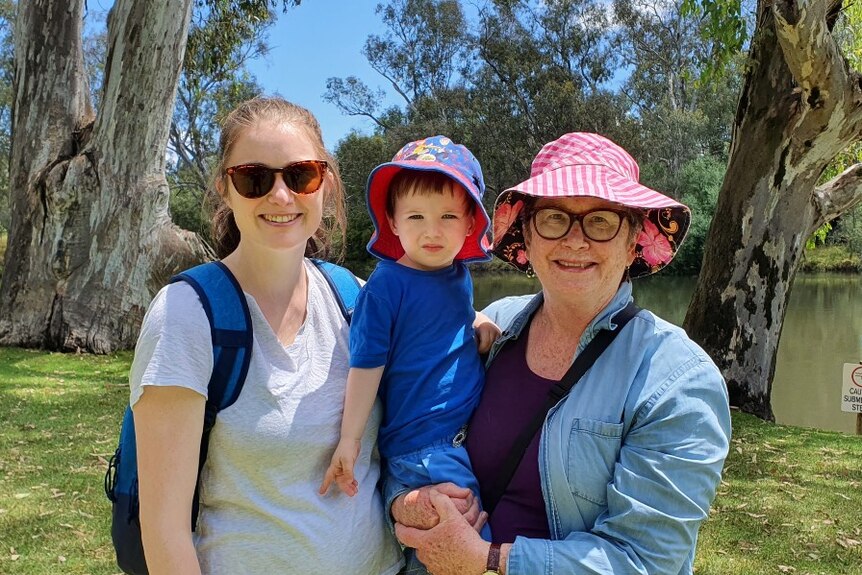 A young woman and her toddler son stand with an older woman on the banks of the Murray River.