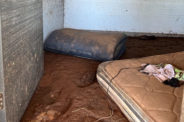 A deep layer of mud covering the floor of a home, with a dirty mattress nearby.