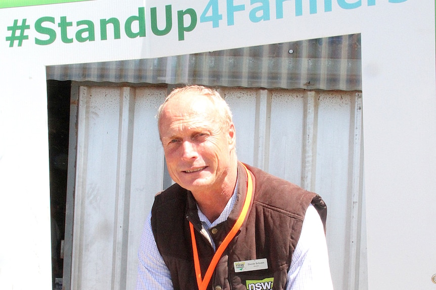 A man stands in front of a sign that says stand up for farmers