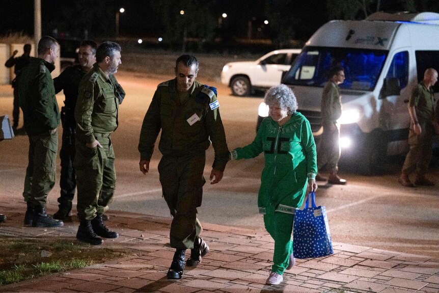 An elderly woman walking next to a man in military uniform.