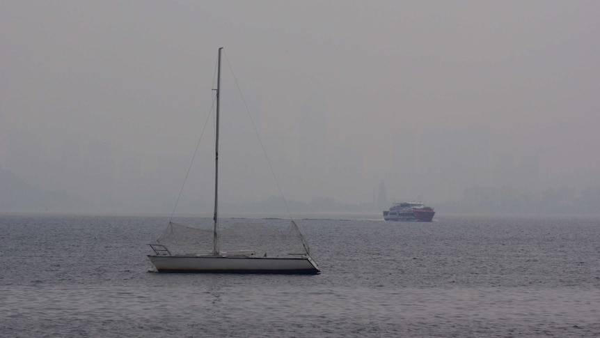 A yacht on water in front of the Perth CBD, which has been obscured by smoke.