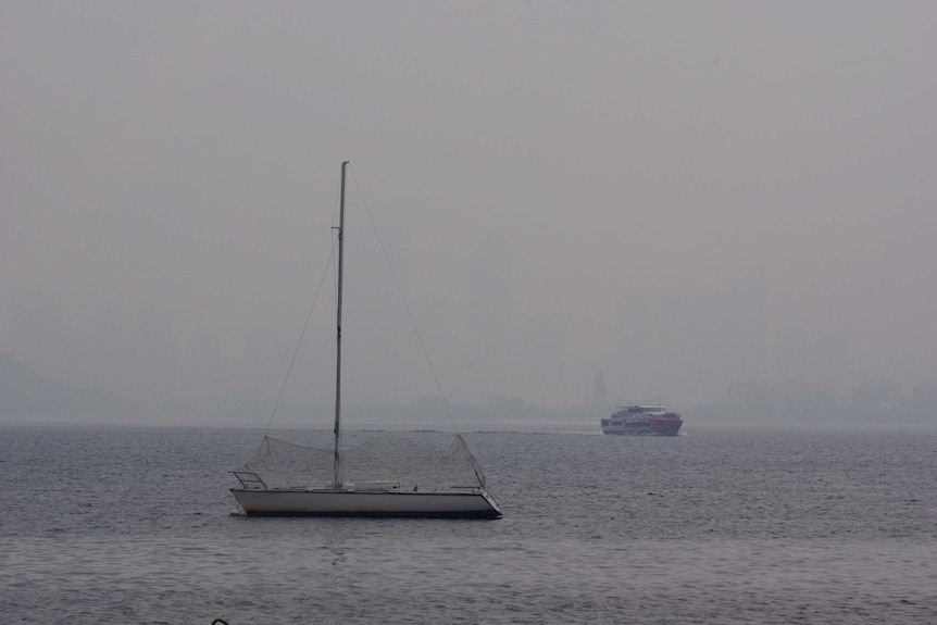 A yacht on water in front of the Perth CBD, which has been obscured by smoke.