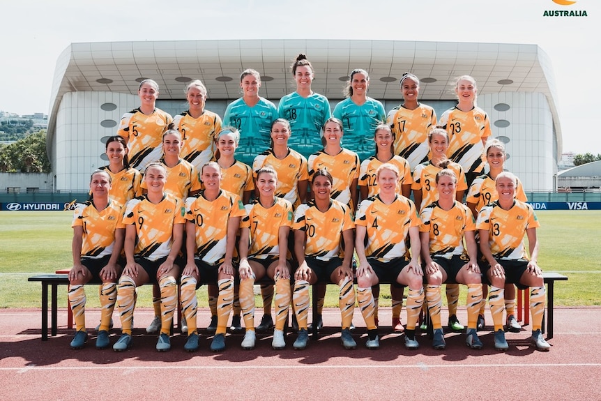 A women's soccer team wearing yellow green and white poses for a photo