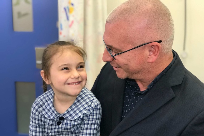 A girl in a school uniform sits on her father's lap