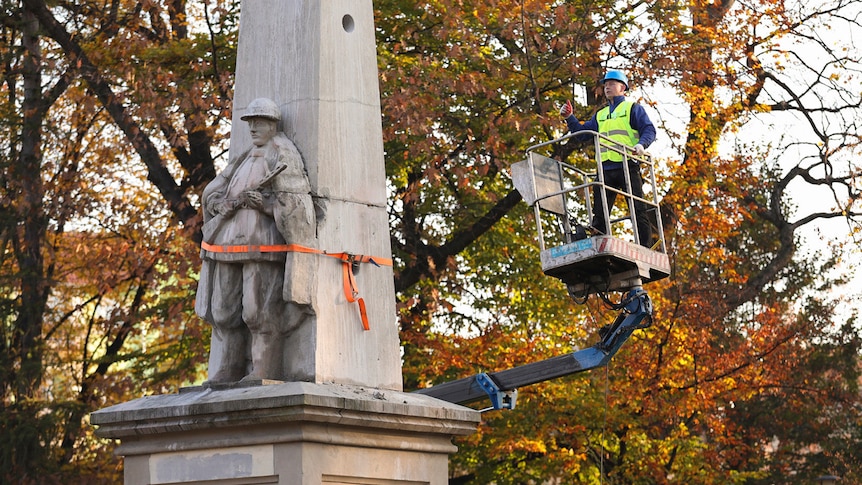 A man on a cherry picker beside a statue wrapped in tape