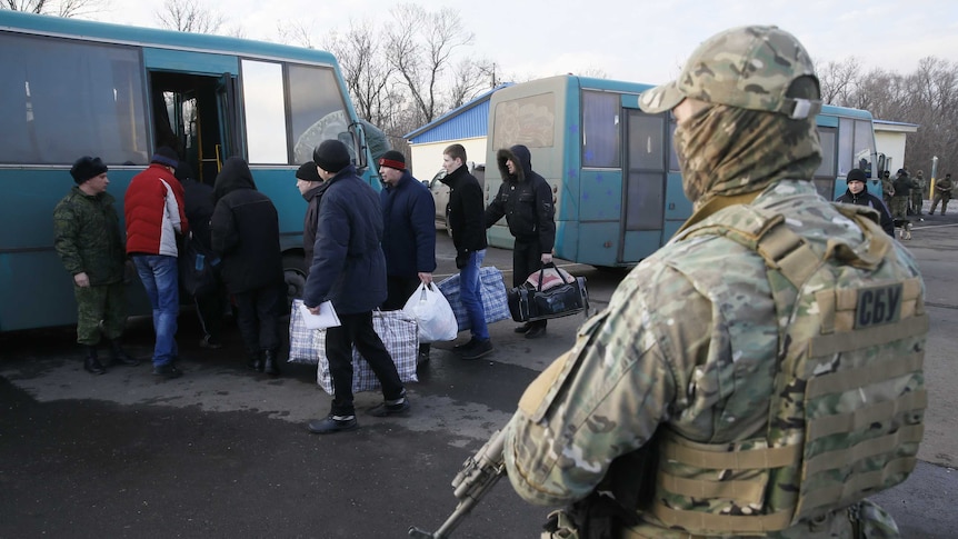 Prisoners board a bus while armed soldiers watch on.