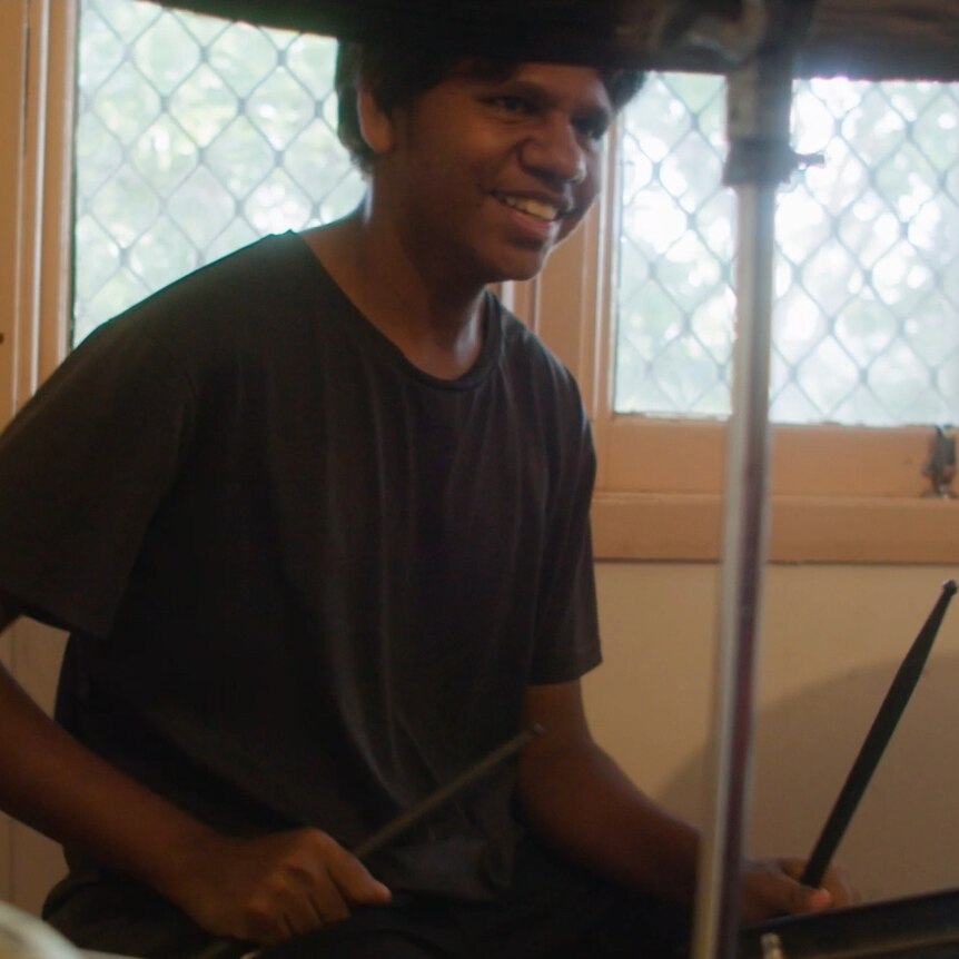 A young man sits a drum kit holding drum sticks
