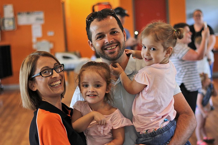 A family smiling shot - mum holds one daughter and dad holds the other daughter.